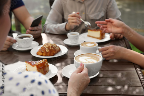 Fototapeta Naklejka Na Ścianę i Meble -  Friends drinking coffee at wooden table in outdoor cafe, closeup