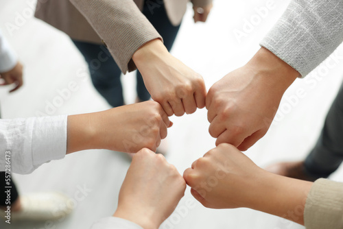 Group of people holding fists together indoors, above view. Unity concept