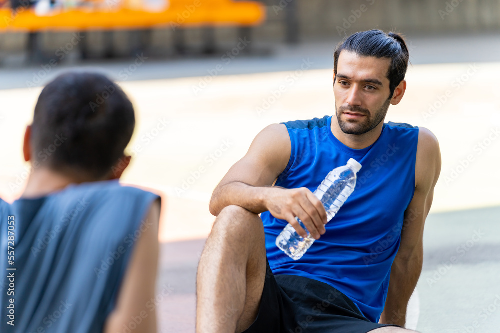 Two man friends athlete resting and drinking water together after play streetball on outdoors court in sunny day. Sportsman basketball player do sport training workout at street court in the city. Two man friends athlete resting and drinking water together after play streetball on outdoors court in sunny day. Sportsman basketball player do sport training workout at street court in the city.