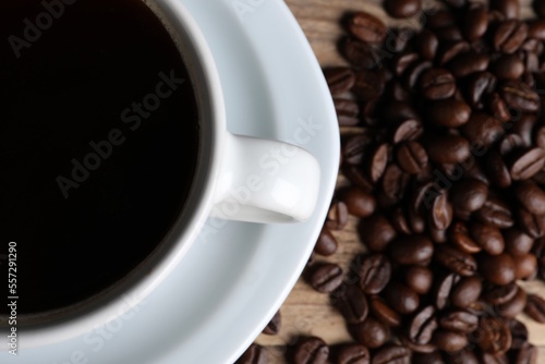 Cup of hot aromatic coffee and roasted beans on wooden table, top view. Space for text