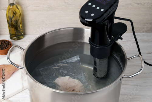 Thermal immersion circulator and vacuum packed meat in pot on white wooden table. Sous vide cooking