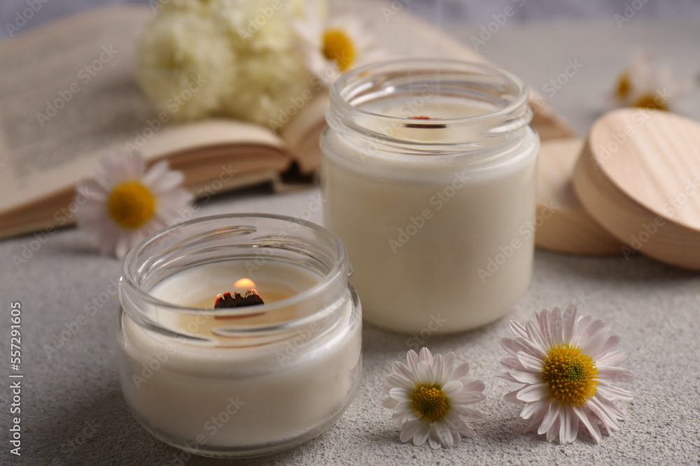 Burning scented candles and chamomile flowers on light gray textured table, closeup Burning scented candles and chamomile flowers on light gray textured table, closeup