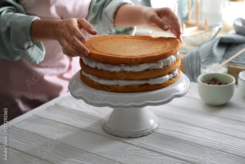 Woman stacking homemade sponge cakes at white wooden table, closeup