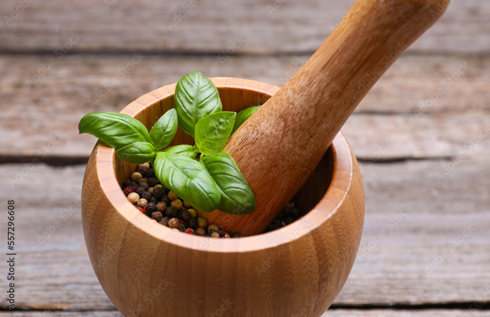 Mortar with peppercorns and basil on wooden table, closeup