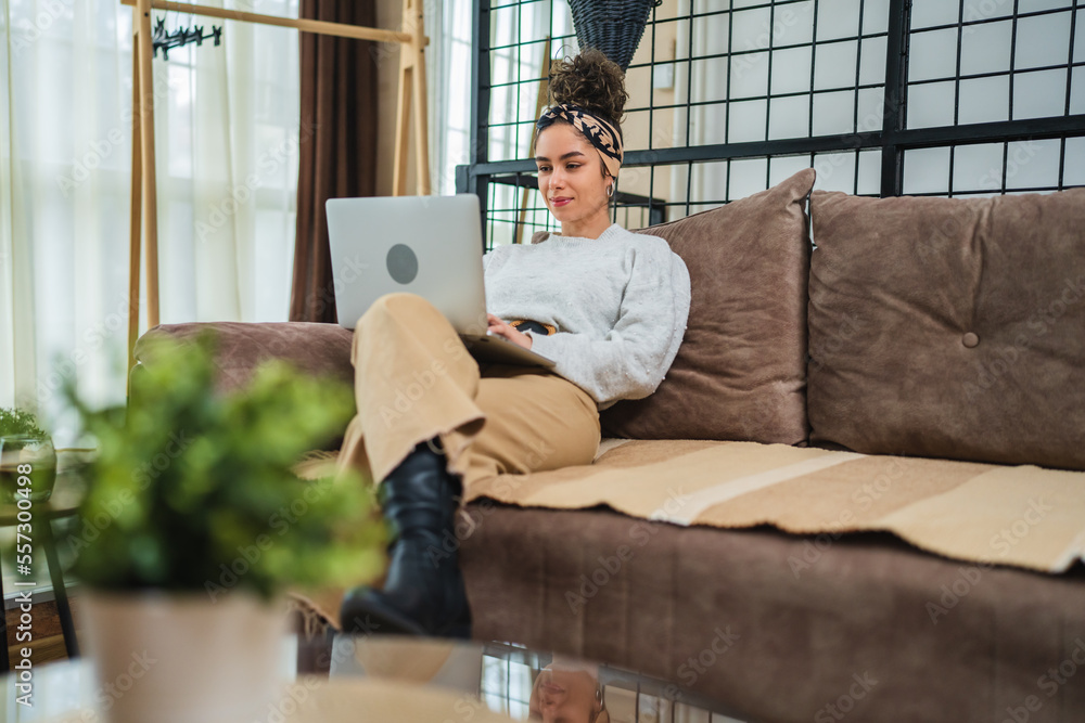 A young girl studying or doing business from her home while sitting on sofa and working on her laptop and drinking coffee during the day