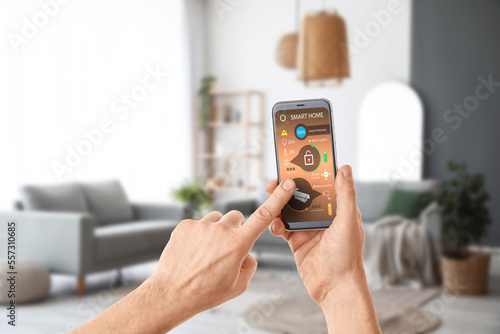 Man's hands holding mobile phone with smart home security system on screen in living room