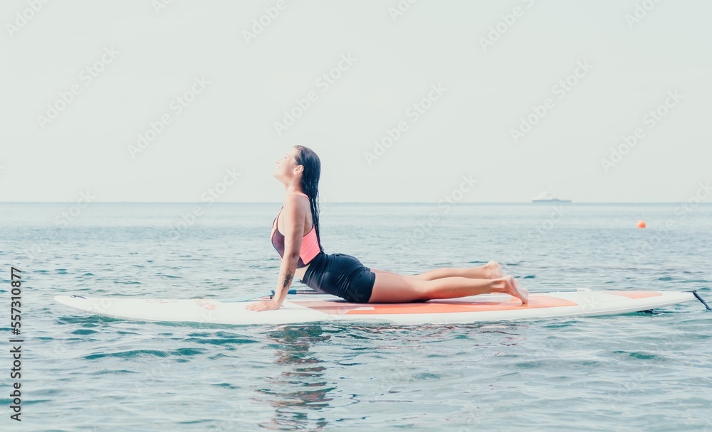 Woman sup yoga. Happy young sporty woman practising yoga pilates on paddle sup surfboard. Female stretching doing workout on sea water. Modern individual female outdoor summer sport activity.
