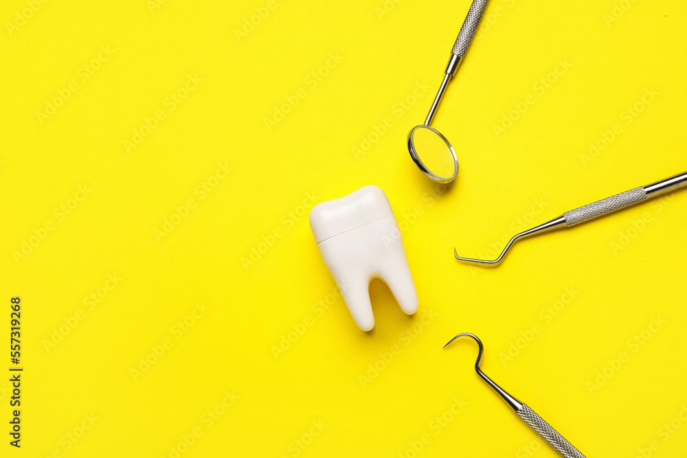 Plastic tooth with dental tools on yellow background Plastic tooth with dental tools on yellow background