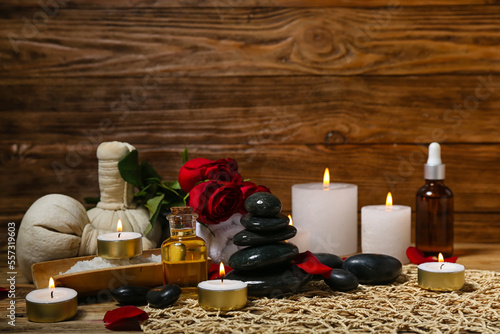 Spa stones with burning candles and roses on wooden table, closeup. Valentine's Day celebration