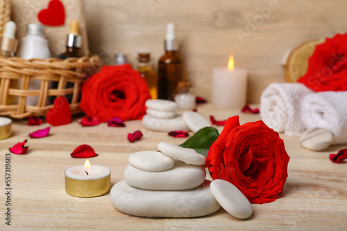 Spa stones with rose and candle on wooden table  closeup. Valentine s Day celebration