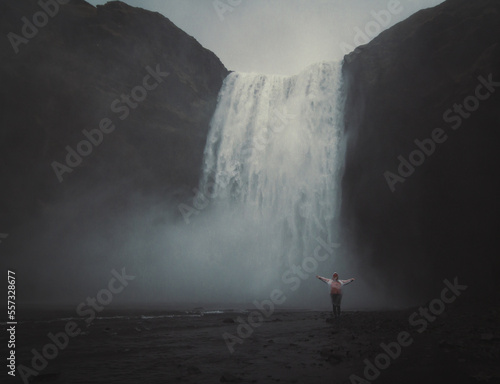 Brave person near waterfall landscape photo. Beautiful nature scenery photography with grey sky on background. Idyllic scene. High quality picture for wallpaper, travel blog, magazine, article