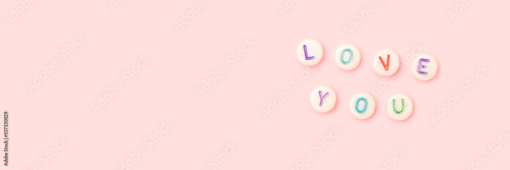 Love you. Banner with quote made of white round beads with colorful letters on a pink pastel background. Valentines Day concept.