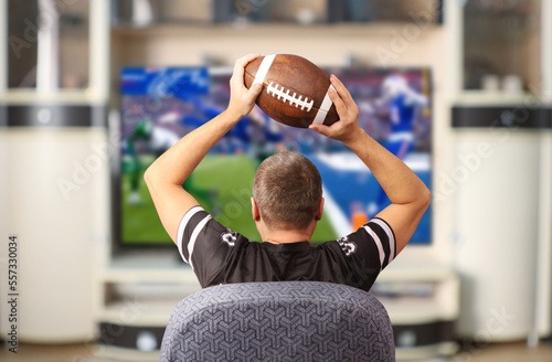 Fan of american football. Man with a ball watching TV. photo