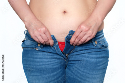 Overweight and diet, woman in unbuttoned jeans with naked belly. Weight loss concept, slimming and obesity