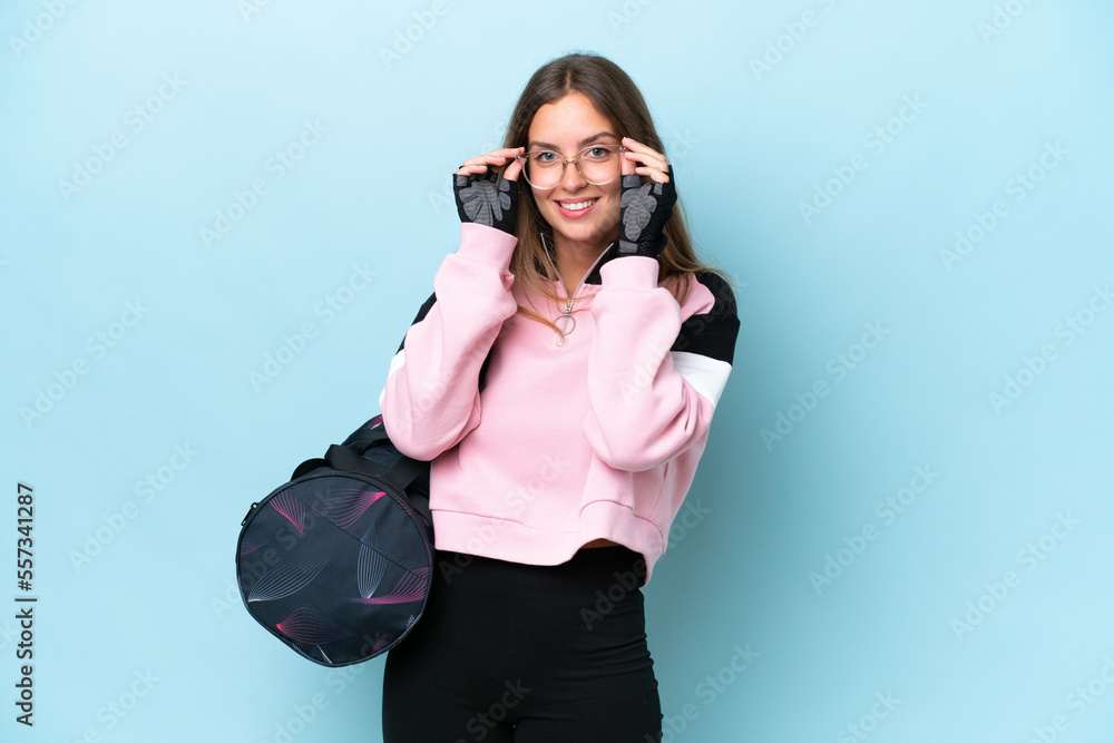 Young sport woman with sport bag isolated on blue background with glasses and surprised