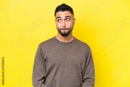 Young Arab handsome man isolated on yellow background having doubts while looking up