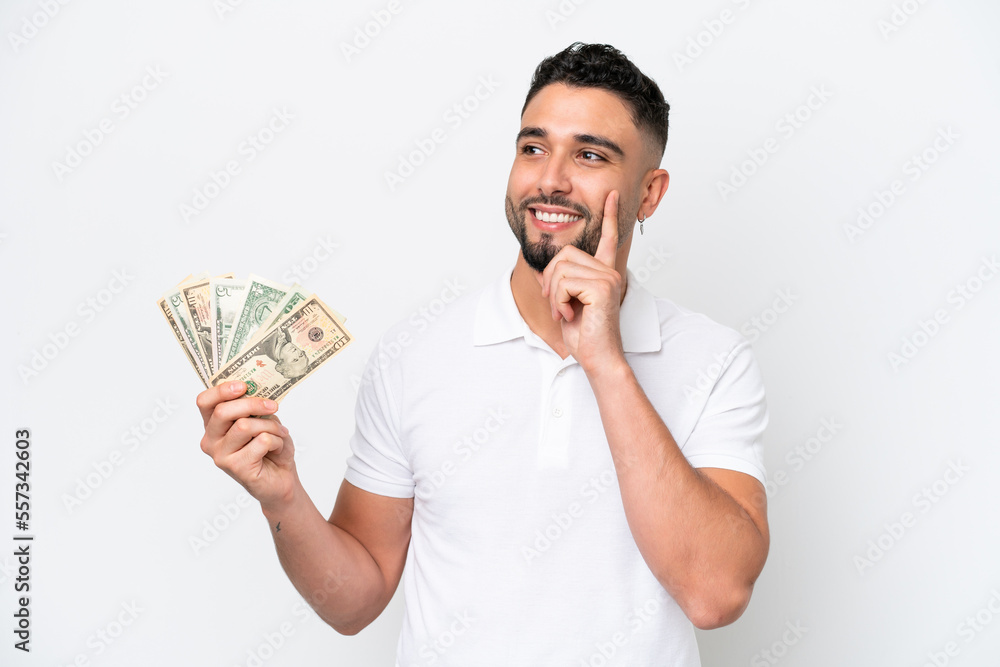Young Arab man taking a lot of money isolated on white background thinking an idea while looking up Young Arab man taking a lot of money isolated on white background thinking an idea while looking up
