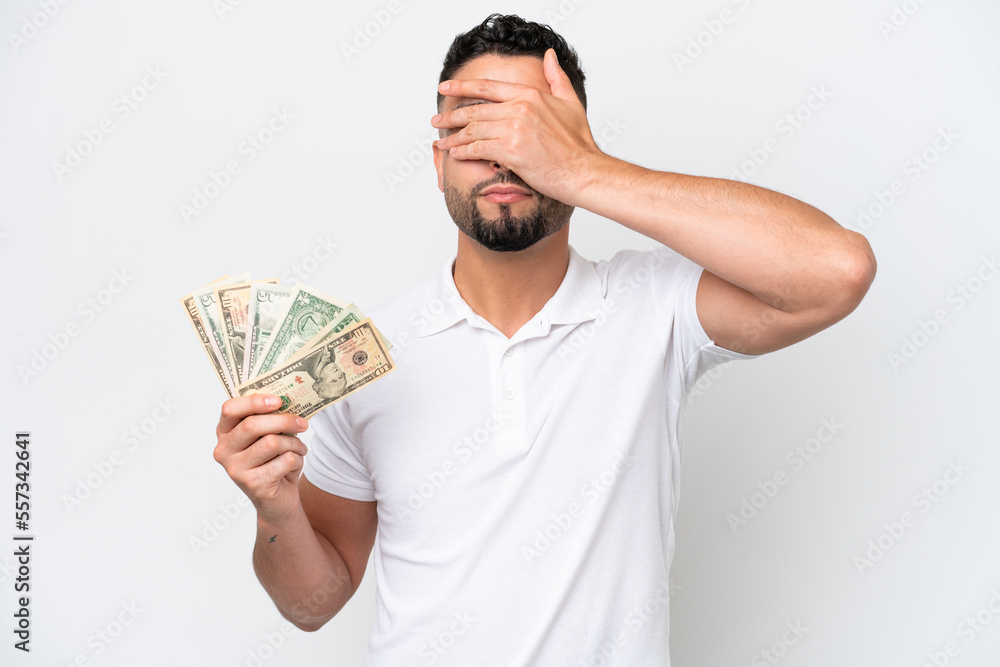 Young Arab man taking a lot of money isolated on white background covering eyes by hands. Do not want to see something Young Arab man taking a lot of money isolated on white background covering eyes by hands. Do not want to see something