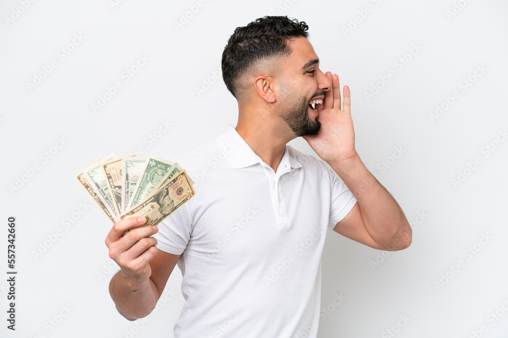Young Arab man taking a lot of money isolated on white background shouting with mouth wide open to the side Young Arab man taking a lot of money isolated on white background shouting with mouth wide open to the side