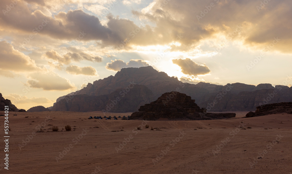 Panoramic sunset view of Wadi Rum desert in Jordan with clouds moving over flat sand landscape with mountains in background, 