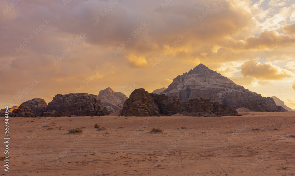 Panoramic sunset view of Wadi Rum desert in Jordan with clouds moving over flat sand landscape with mountains in background, 