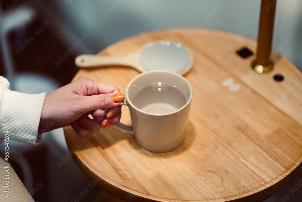 Female hand picking up glass of water on wooden table in modern style