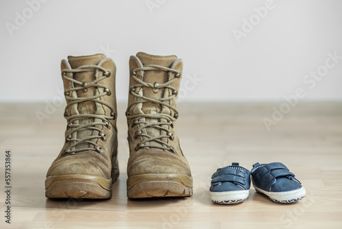 old worn military boots and baby shoes on wooden floor. Concept of military father and family.