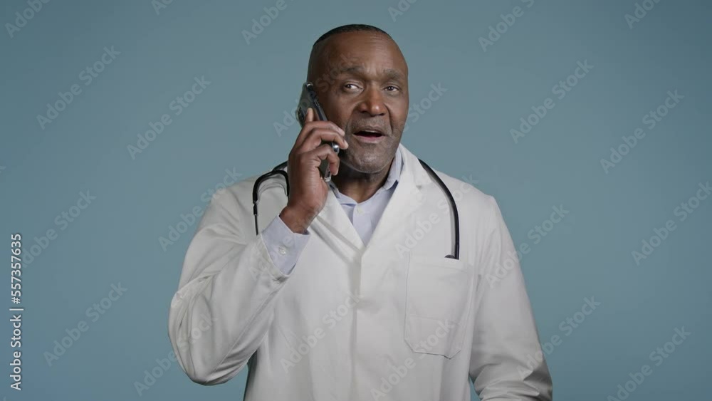 Mature smiling man standing in studio on gray background male doctor professional medical worker talk on mobile phone with patient distance consulting hospital client using smartphone remote diagnosis Mature smiling man standing in studio on gray background male doctor professional medical worker talk on mobile phone with patient distance consulting hospital client using smartphone remote diagnosis