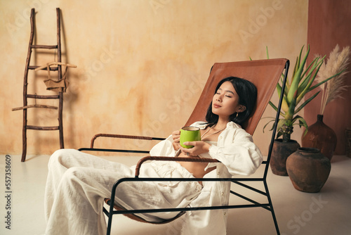 Fototapeta Asian girl relaxing on lounger with mug of tea, meditating, spending weekend on