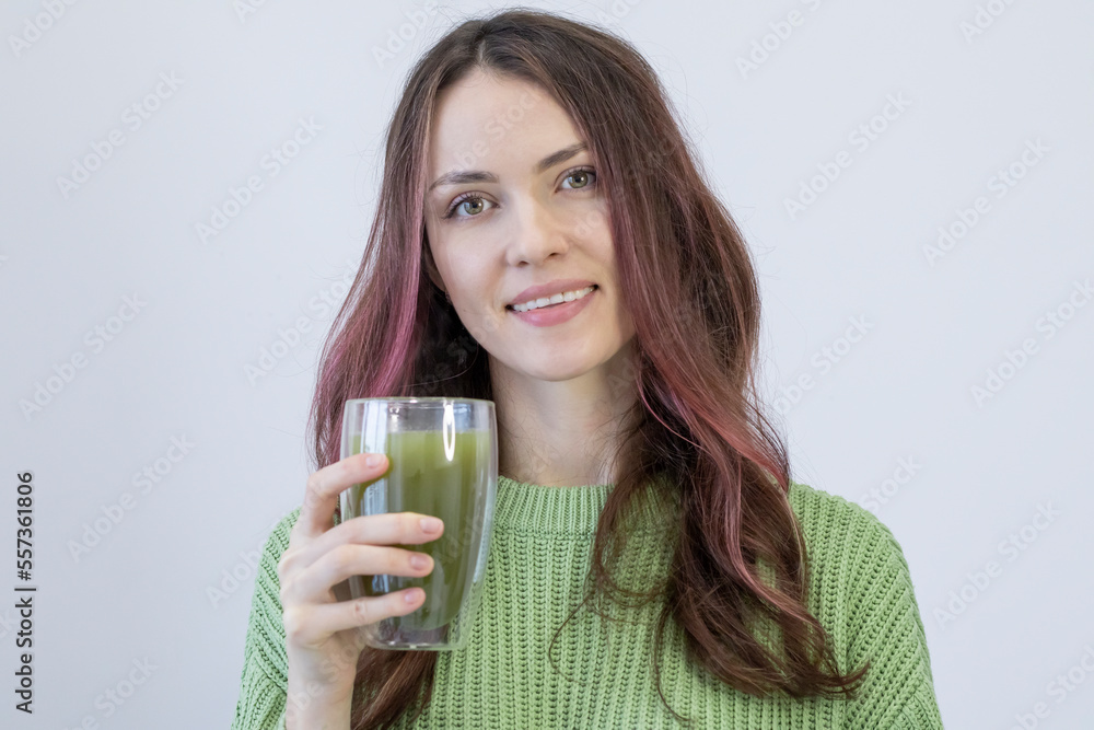 Beautiful young woman with a big smile holds a green matcha tea in her hand and looks straight into the camera. Beautiful young woman with a big smile holds a green matcha tea in her hand and looks straight into the camera.