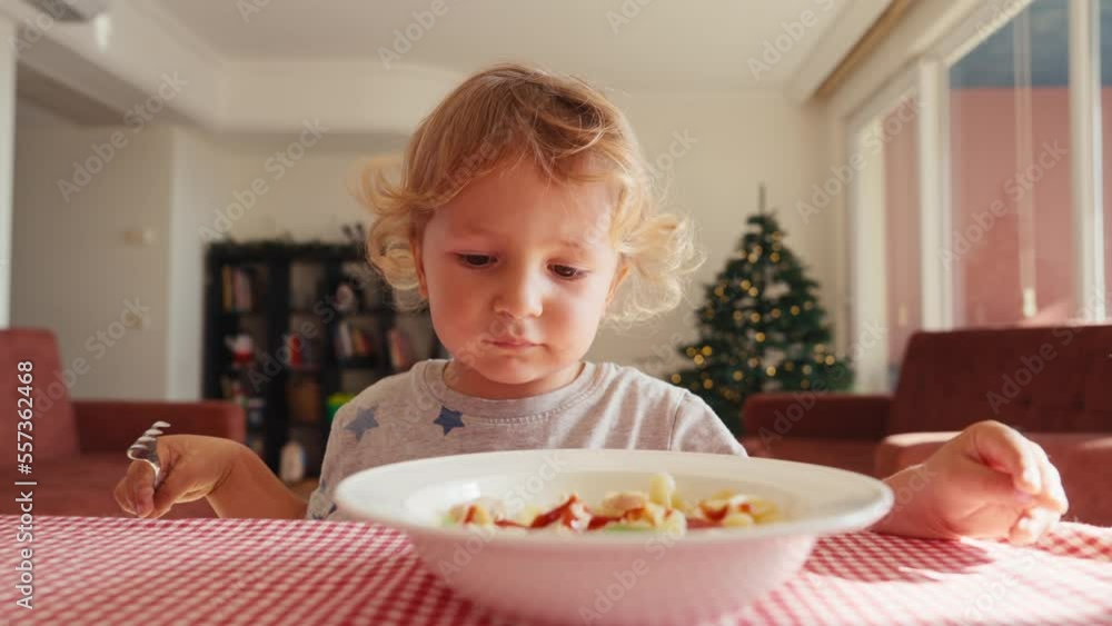The child in the kitchen at the table eating macaroni with ketchup. Mother adds ketchup to the child. Bad eating habits. The child in the kitchen at the table eating macaroni with ketchup. Mother adds ketchup to the child. Bad eating habits.