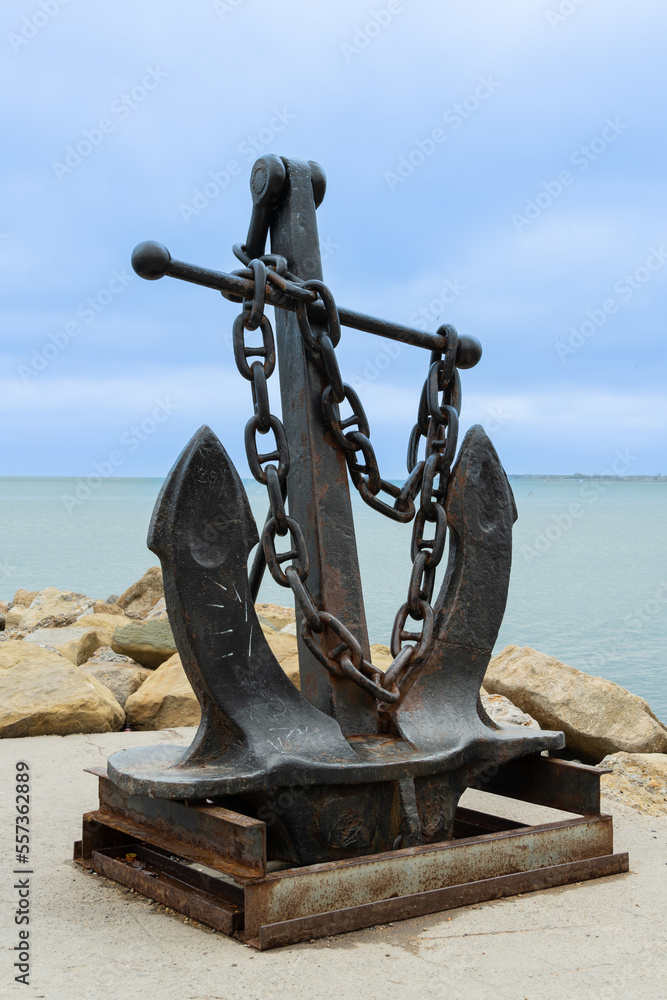 Fototapeta premium Admiralty anchor on pedestal on embankment of resort town. In background,turquoise December sea. Gelendzhik bay. Selective focus. Blurred background. Close-up. Gelendzhikk, Russia - December 13, 2022