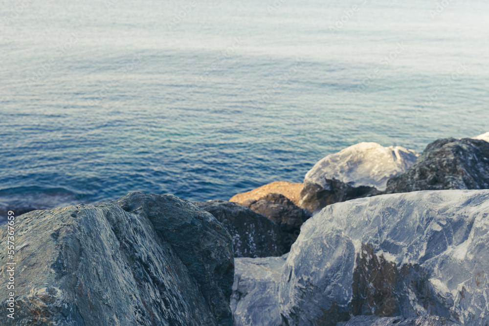 Close up of big stones of mediterranean sea shoe. Stone wave breakers of Italian coast on a sunny summer day. Genoa, region of Liguria, Italy. Flat serene sea landscape. Close up of big stones of mediterranean sea shoe. Stone wave breakers of Italian coast on a sunny summer day. Genoa, region of Liguria, Italy. Flat serene sea landscape.