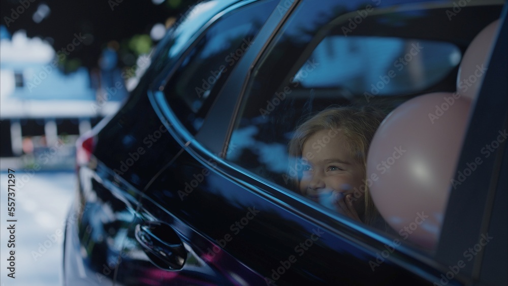 Happy positive birthday girl riding on a back seat of a car surrounded with balloons