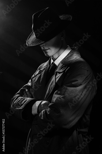 a dark silhouette of a man in a raincoat and hat with his head down in the style of crime noir. A dramatic noir portrait in the style of detectives of the 1950s.