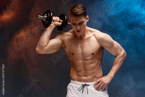 Front image of fit, strong young man with bare torso, training with dumb-bell, showing abs