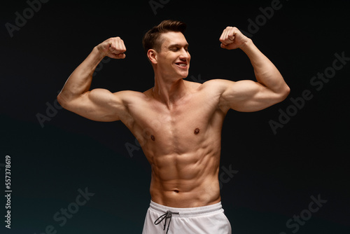 Happy athletic model demonstrating biceps while posing with naked torso