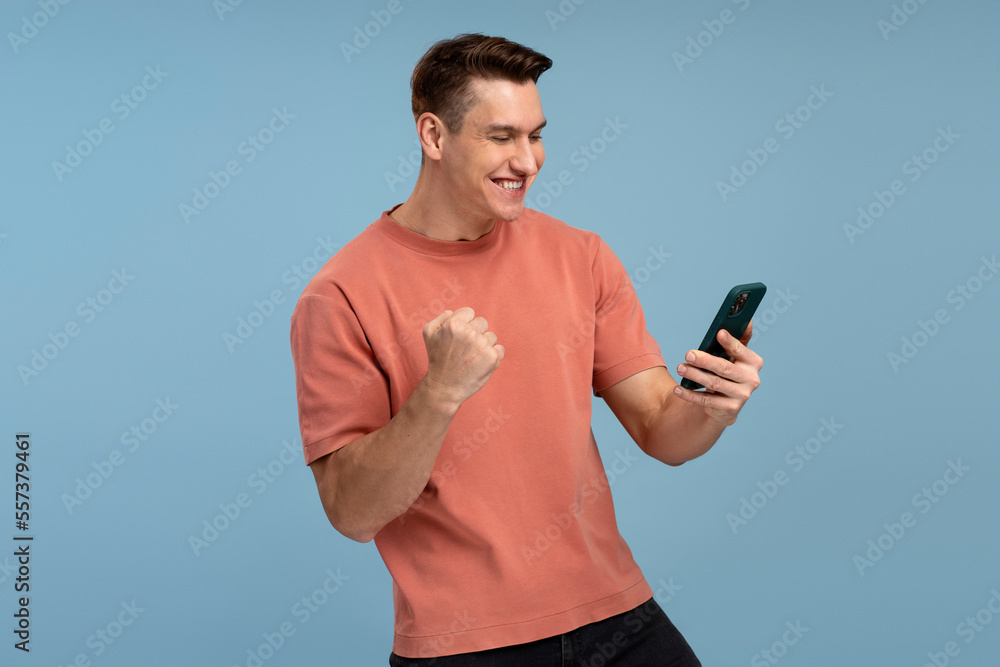 Happy satisfied man in t shirt holding smartphone and smiling making yes gesture Happy satisfied man in t shirt holding smartphone and smiling making yes gesture