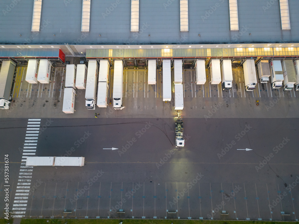Aerial view of goods warehouse night. Logistics delivery; center in industrial city zone from above. Aerial view of trucks loading at logistic center. View from drone.