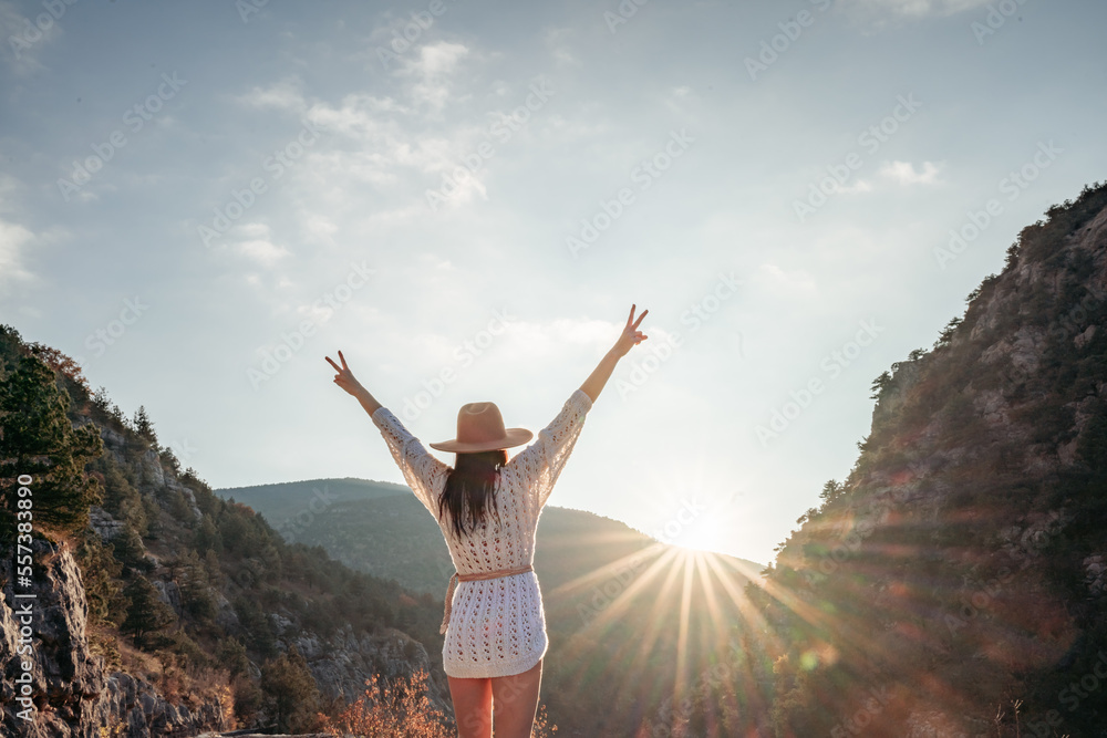 Fototapeta premium Traveler woman in brown hat and white sweater looking at amazing mountains and forest, wanderlust travel concept, atmospheric epic moment