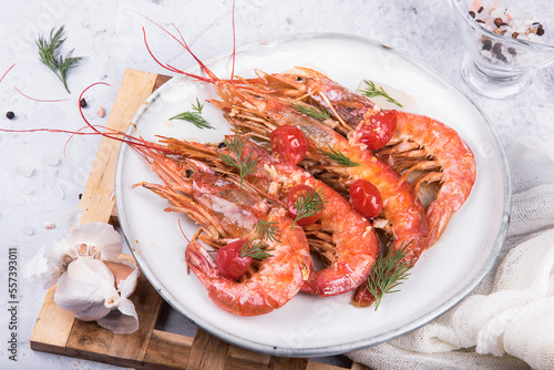 Baked langoustines in garlic sauce with cherry tomatoes on a white plate on a marble background, side view.
