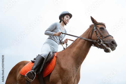 Asian equestrian athlete riding horse holding reins on outdoor background