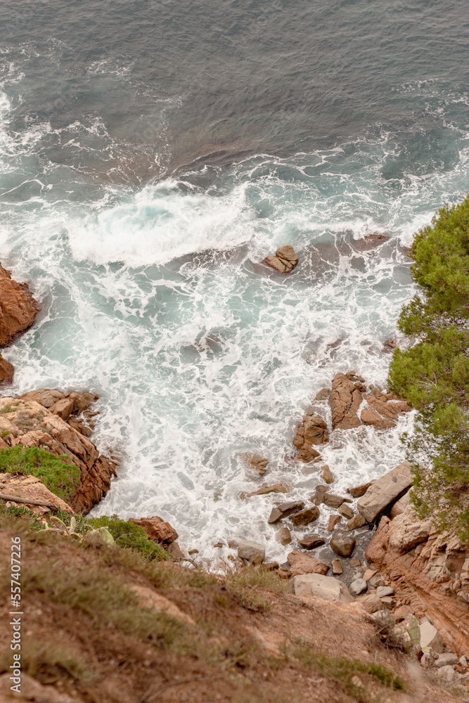 Obraz premium La espuma del mar Mediterráneo formándose al romper las olas contra las rocas de los acantilado de las murallas del pueblo catalan Tossa de Mar.