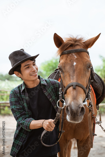 asian man in cowboy hat leads the horse's head on the leash at the ranch