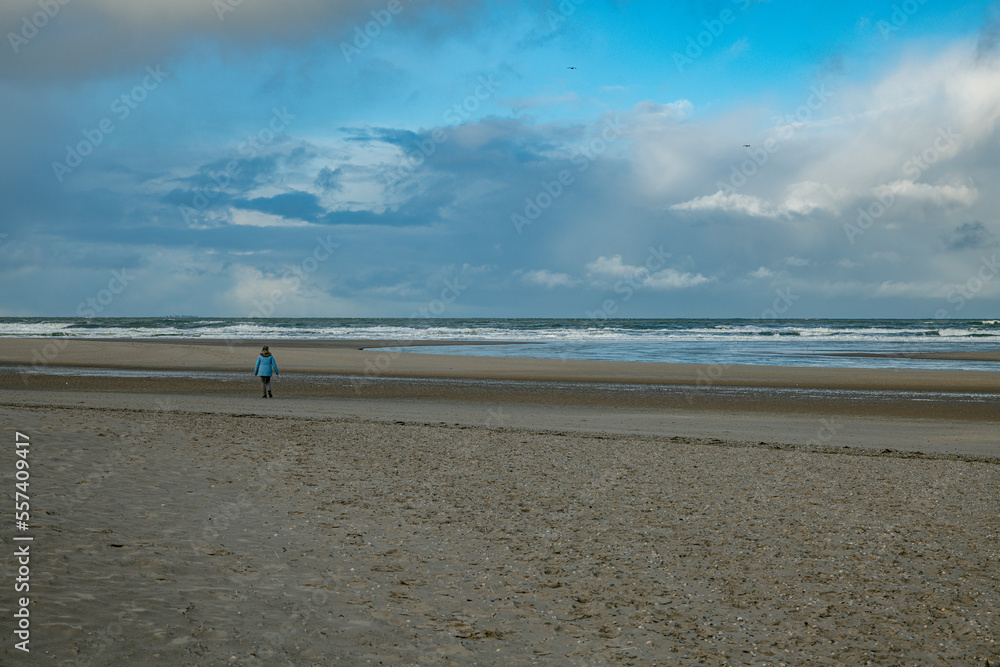 a woman walks alone on the wide beach with the sea in the background