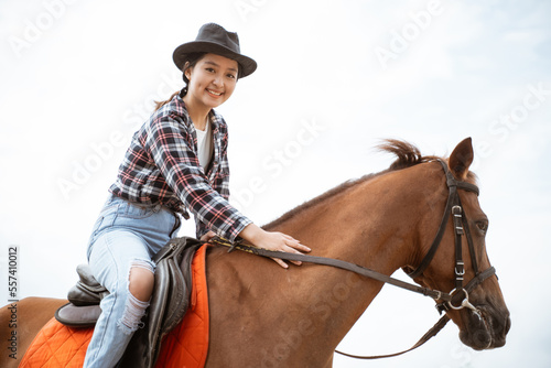 beautiful woman in cowboy hat holding reins sitting on horse at ranch