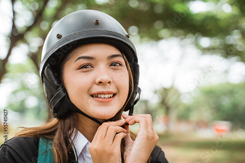 Asian student girl wearing helmet strap while riding motorbike to school