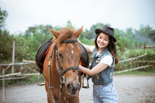 beautiful asian cowboy girl standing beside horse on outdoor background © Odua Images