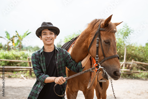 man in cowboy hat smiling while stroking the head of a horse at the ranch