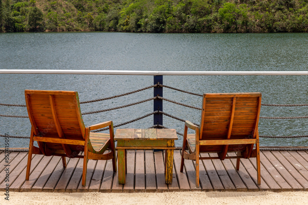 Two empty chairs and small wooden table facing view with beautiful lake and mountains Two empty chairs and small wooden table facing view with beautiful lake and mountains